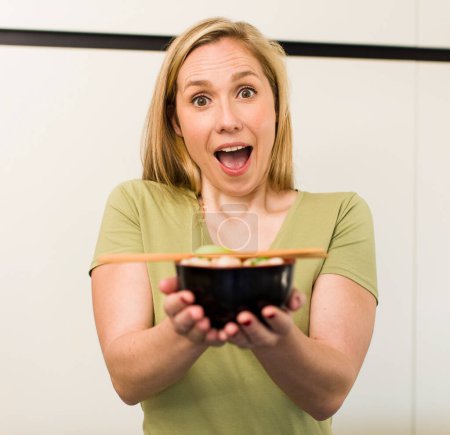 Téléchargez les photos : Young adult pretty blonde woman eating a ramen noodles bowl - en image libre de droit