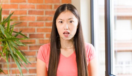 Téléchargez les photos : Asian pretty woman at home against brick wall with a plant - en image libre de droit