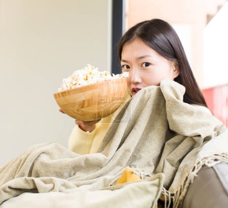 Photo for Asian pretty woman eating popcorns and watching a film at home - Royalty Free Image