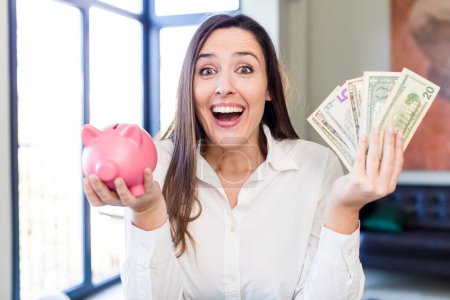 Foto de Young adult pretty woman with a piggy bank. money and savings concept - Imagen libre de derechos