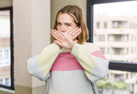 Foto de Pretty caucasian woman covering face with hand and putting other hand up front to stop camera, refusing photos or pictures. home interior concept - Imagen libre de derechos