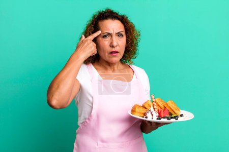 Photo for Pretty middle age woman feeling confused and puzzled, showing you are insane. home made waffles concept - Royalty Free Image