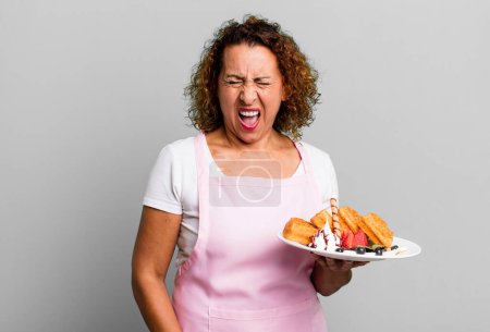 Photo for Pretty middle age woman shouting aggressively, looking very angry. home made waffles concept - Royalty Free Image