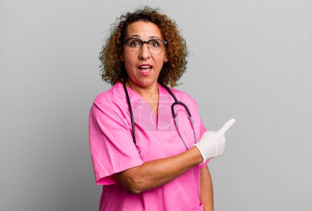 Photo for Pretty middle age woman looking excited and surprised pointing to the side. nurse concept - Royalty Free Image