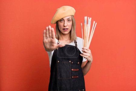 Photo for Pretty blonde woman looking serious showing open palm making stop gesture. painter artist concept - Royalty Free Image