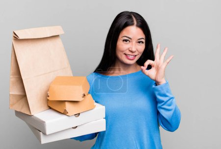 Téléchargez les photos : Hispanic pretty woman feeling happy, showing approval with okay gesture. with take away fast food packages - en image libre de droit