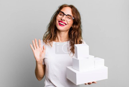 Photo for Hispanic pretty woman smiling happily, waving hand, welcoming and greeting you. with white boxes packages - Royalty Free Image