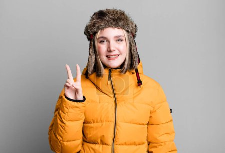Foto de Young pretty woman smiling and looking friendly, showing number two. cold and coat concept - Imagen libre de derechos