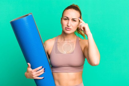 Photo for Young pretty woman feeling confused and puzzled, showing you are insane. fitness and yoga concept - Royalty Free Image