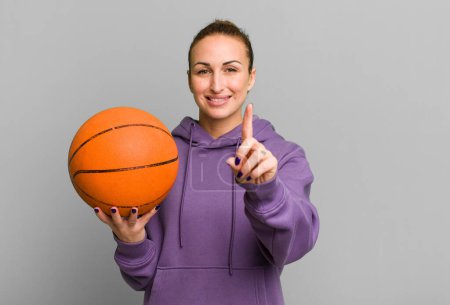 Téléchargez les photos : Young pretty woman smiling and looking friendly, showing number one. basketball concept - en image libre de droit