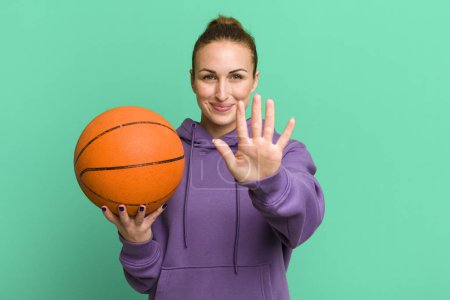 Téléchargez les photos : Young pretty woman smiling and looking friendly, showing number five. basketball concept - en image libre de droit