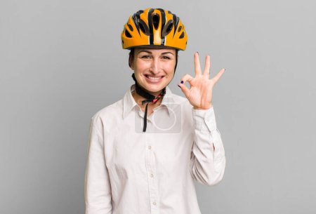 Photo for Young pretty woman feeling happy, showing approval with okay gesture. business and bike concept - Royalty Free Image