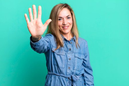 Photo for Blonde adult woman smiling and looking friendly, showing number five or fifth with hand forward, counting down - Royalty Free Image