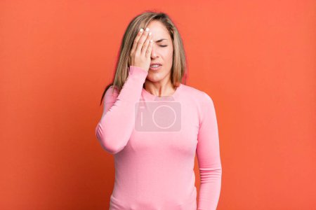 Photo for Blonde adult woman looking sleepy, bored and yawning, with a headache and one hand covering half the face - Royalty Free Image