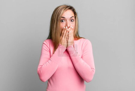 Foto de Blonde adult woman happy and excited, surprised and amazed covering mouth with hands, giggling with a cute expression - Imagen libre de derechos