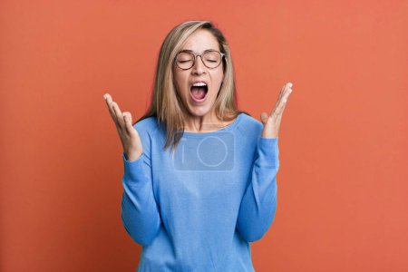 Photo for Blonde adult woman furiously screaming, feeling stressed and annoyed with hands up in the air saying why me - Royalty Free Image