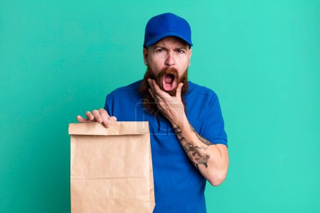 Photo for Young adult red hair bearded cool delivery man with a paper bag - Royalty Free Image