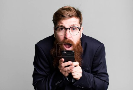 Téléchargez les photos : Jeune adulte cheveux roux barbu cool homme d'affaires en utilisant son smartphone - en image libre de droit