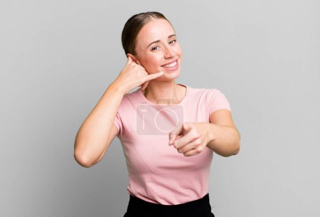 Photo for Smiling cheerfully and pointing to camera while making a call you later gesture, talking on phone - Royalty Free Image
