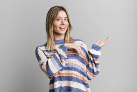 Photo for Blonde pretty woman smiling cheerfully and pointing to copy space on palm on the side, showing or advertising an object - Royalty Free Image