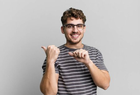 Photo for Young adult caucasian man smiling cheerfully and casually pointing to copy space on the side, feeling happy and satisfied - Royalty Free Image