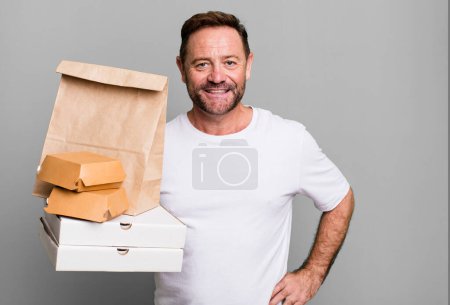 Foto de Hombre de mediana edad sonriendo felizmente con una mano en la cadera y confiado. entrega y comida rápida para llevar concepto - Imagen libre de derechos