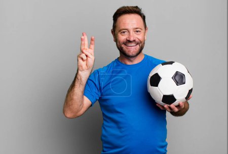 Téléchargez les photos : Middle age man smiling and looking friendly, showing number three. with a soccer ball. fitness concept - en image libre de droit