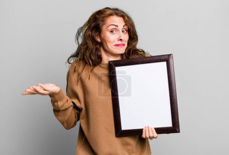 Photo for Hispanic pretty woman feeling puzzled and confused and doubting with an empty blank frame - Royalty Free Image
