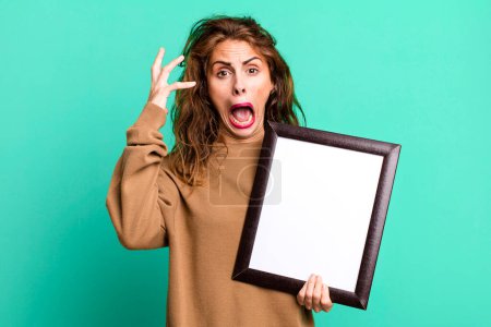 Photo for Hispanic pretty woman screaming with hands up in the air with an empty blank frame - Royalty Free Image