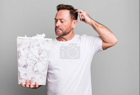 Photo for Middle age man smiling happily and daydreaming or doubting. paper balls trash basket - Royalty Free Image