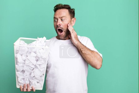 Photo for Middle age man feeling happy, excited and surprised. paper balls trash basket - Royalty Free Image