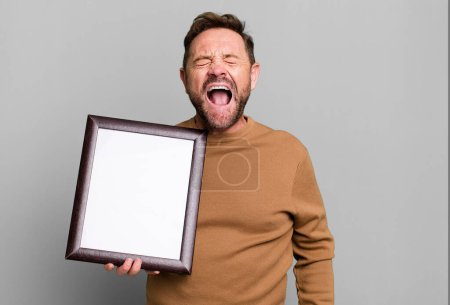Photo for Middle age man shouting aggressively, looking very angry with an empty frame - Royalty Free Image