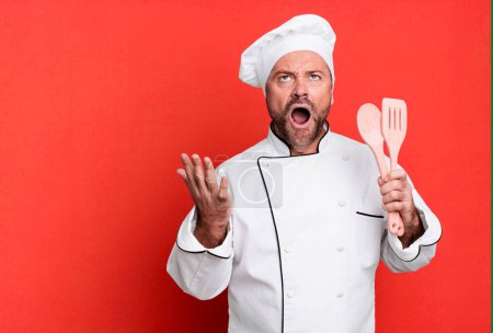 Photo for Middle age man looking desperate, frustrated and stressed. chef and tools concept - Royalty Free Image