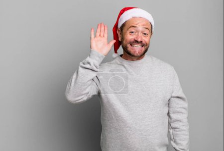 Téléchargez les photos : Homme d'âge moyen souriant joyeusement, main agitant, vous accueillant et vous saluant. concept de Noël - en image libre de droit