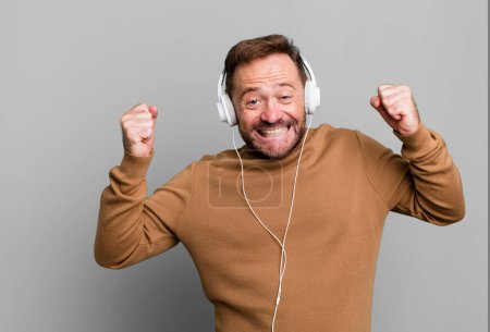 Téléchargez les photos : Homme d'âge moyen écouter de la musique avec son casque sport coach concept avec un ballon de football - en image libre de droit