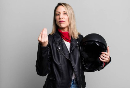Téléchargez les photos : Pretty blonde woman making capice or money gesture, telling you to pay. motorbike rider and helmet concept - en image libre de droit