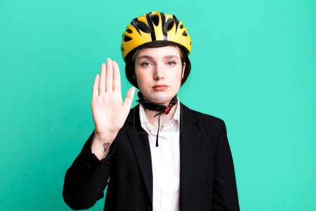 Foto de Joven bonita mujer mirando serio mostrando abierta palma haciendo gesto de parada. concepto de bicicleta y mujer de negocios - Imagen libre de derechos