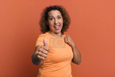 Foto de Mujer hispana de mediana edad sintiéndose orgullosa, despreocupada, segura y feliz, sonriendo positivamente con los pulgares hacia arriba - Imagen libre de derechos