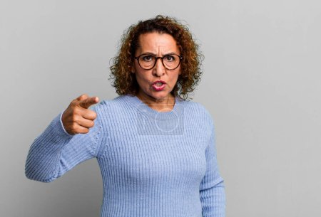 Photo for Middle age hispanic woman pointing at camera with an angry aggressive expression looking like a furious, crazy boss - Royalty Free Image