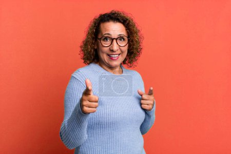 Foto de Mujer hispana de mediana edad sonriendo con una actitud positiva, exitosa y feliz apuntando a la cámara, haciendo letrero con las manos - Imagen libre de derechos