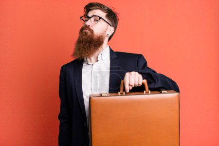 Téléchargez les photos : Jeune adulte cheveux roux barbu homme d'affaires cool avec une valise en cuir - en image libre de droit