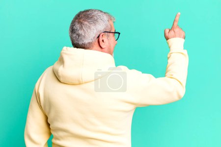 Foto de Hombre mayor de mediana edad de pie y apuntando a objetar en el espacio de copia, vista trasera - Imagen libre de derechos