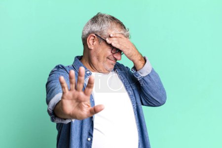 Foto de Hombre mayor de mediana edad cubriendo la cara con la mano y poniendo otra mano por delante para detener la cámara, rechazando fotos o imágenes - Imagen libre de derechos