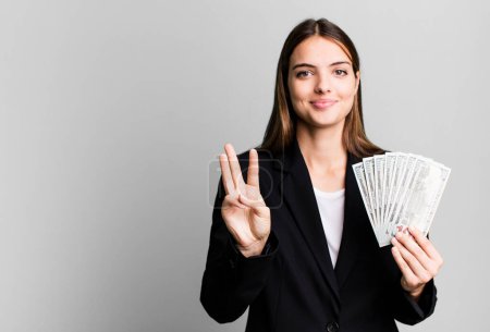Foto de Young pretty woman smiling and looking friendly, showing number three. business and dolla banknotes concept - Imagen libre de derechos