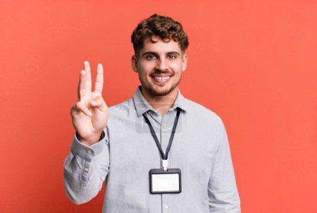 Téléchargez les photos : Jeune homme caucasien adulte souriant et regardant amical, montrant numéro trois. carte d'accréditation vierge ID concept - en image libre de droit
