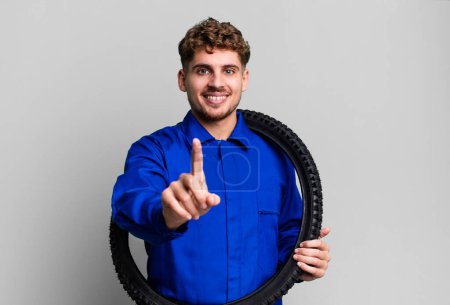 Foto de Young adult caucasian man smiling proudly and confidently making number one. bike repairman or mechanic concept - Imagen libre de derechos