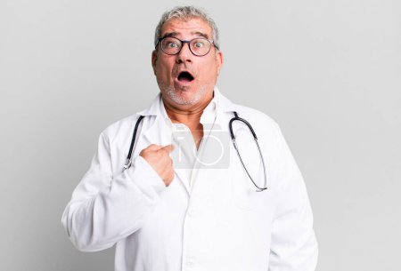 Photo for Middle age senior man looking shocked and surprised with mouth wide open, pointing to self. physician or doctor concept - Royalty Free Image