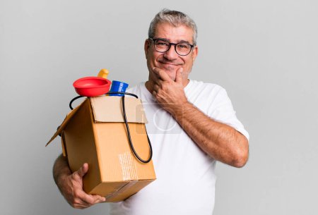 Foto de Hombre mayor de mediana edad sonriendo con una expresión feliz y segura con la mano en la barbilla. ama de llaves reparador con un concepto de caja de herramientas - Imagen libre de derechos