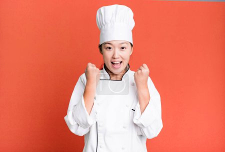 Photo for Pretty asian woman feeling shocked,laughing and celebrating success. restaurant chef concept - Royalty Free Image
