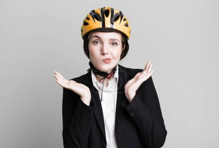 Photo for Young pretty woman feeling puzzled and confused and doubting. bike and businesswoman concept - Royalty Free Image